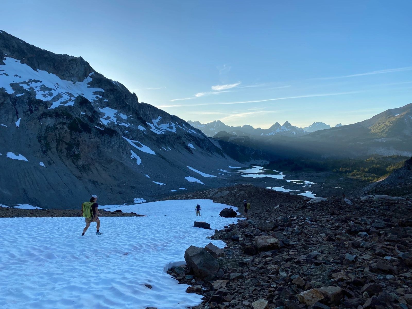 Hikers trekking on a snowy mountain slope during sunset.